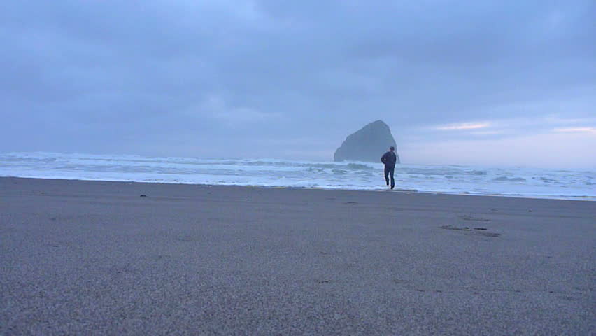 Man running on sandy beach to the Pacific Ocean in Oregon's coastline during