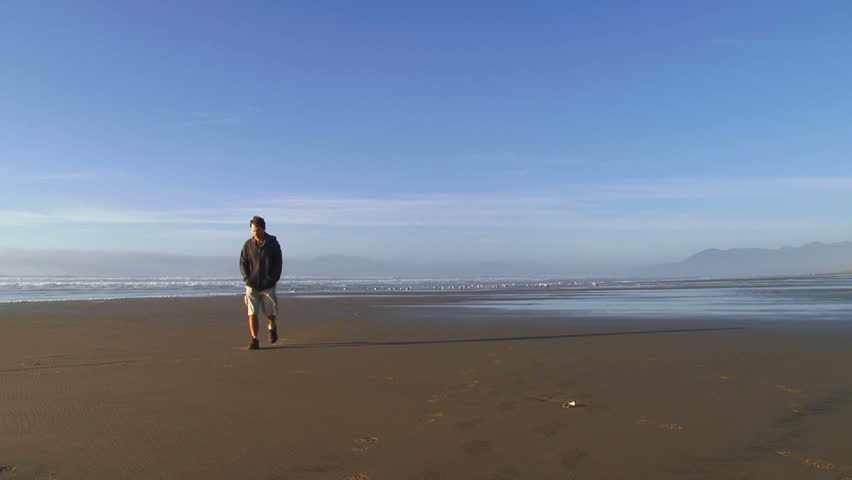 Man walking towards camera on sandy beach in Oregon on a beautiful blue sky day.