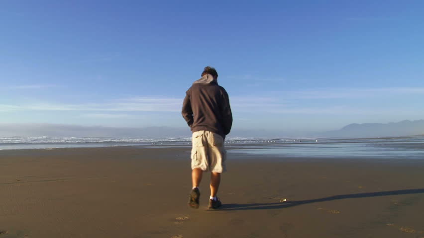 Man walking away on sandy beach in Oregon on a beautiful blue sky day.
