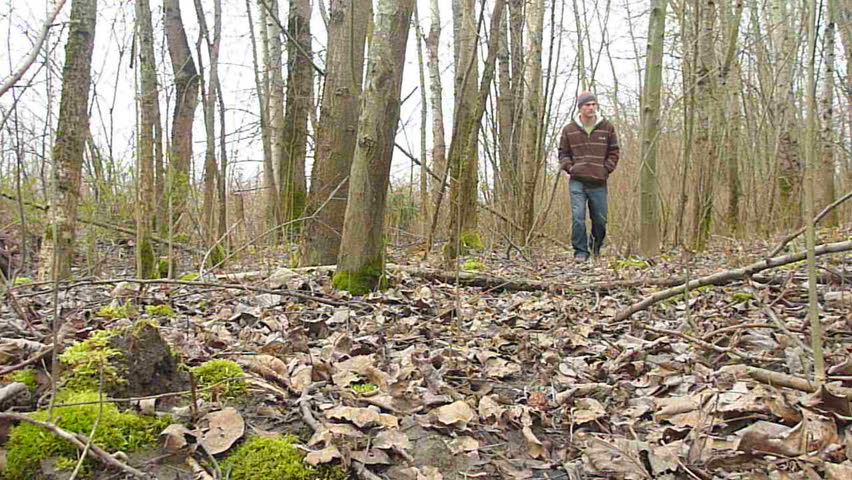 Man walking towards camera in bare forest in winter.