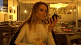 Attractive young woman enjoying a glass of wine in restaurant while chatting on the phone. Selective focus video