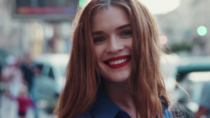 Charming young woman with a magnificent golden hair, big blue eyes, gorgeous red lipstick and stylish look. Attractive young lady is rushing in the city-center, she turns to camera and smiles.