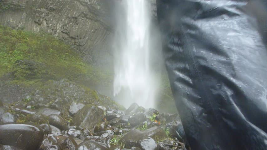 Man walking up to large waterfall in Oregon on rainy day, reaches falls and