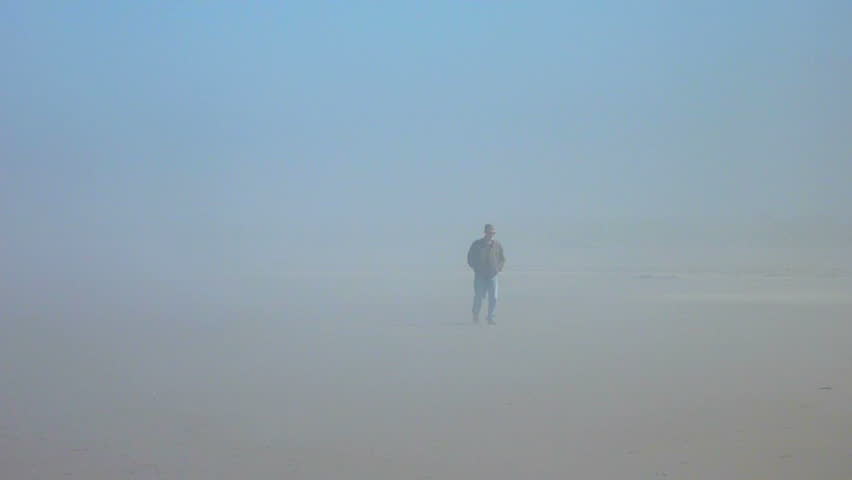 Man walks alone through thick fog at coast.