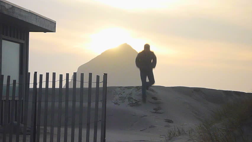 Man walking toward camera near beach house on sandy path to the Pacific Ocean in