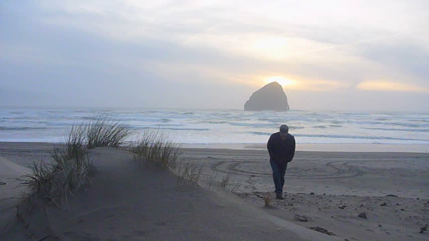 Man walking towards camera on sandy beach by the Pacific Ocean in Oregon's