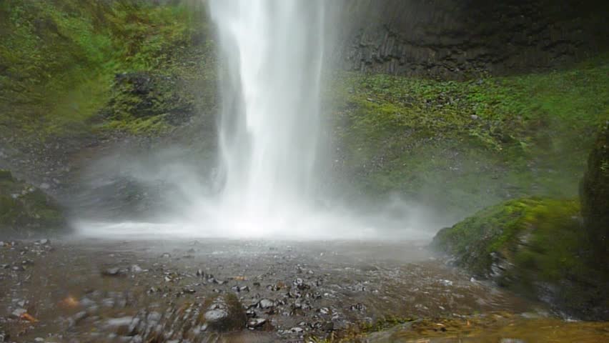 Man walking near large waterfall in Oregon on rainy day reaches falls and lifts