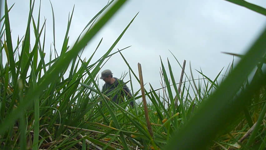 Man walking by camera pulling a river canoe through grass to river on adventure.