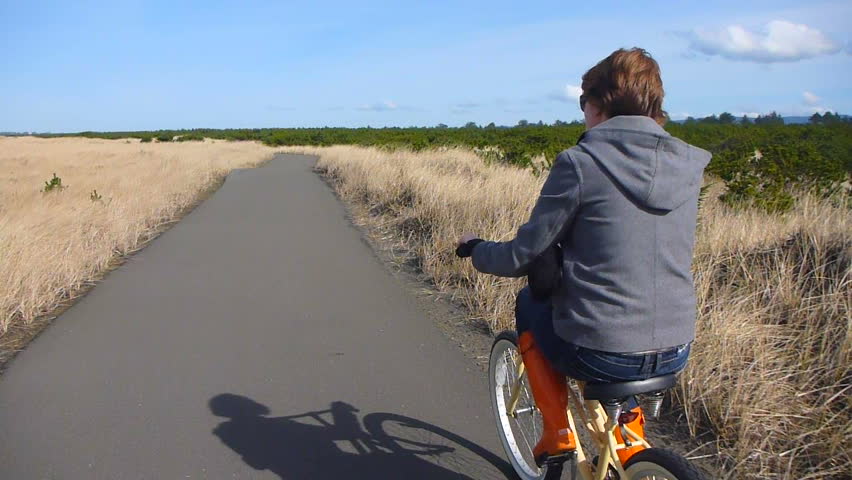 Woman in orange boots pedals beach cruiser bike on paved nature trail in