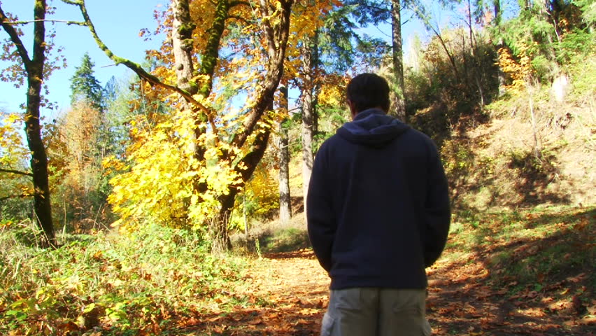 Man walks down forest path full of fallen leaves in Oregon forest in autumn.