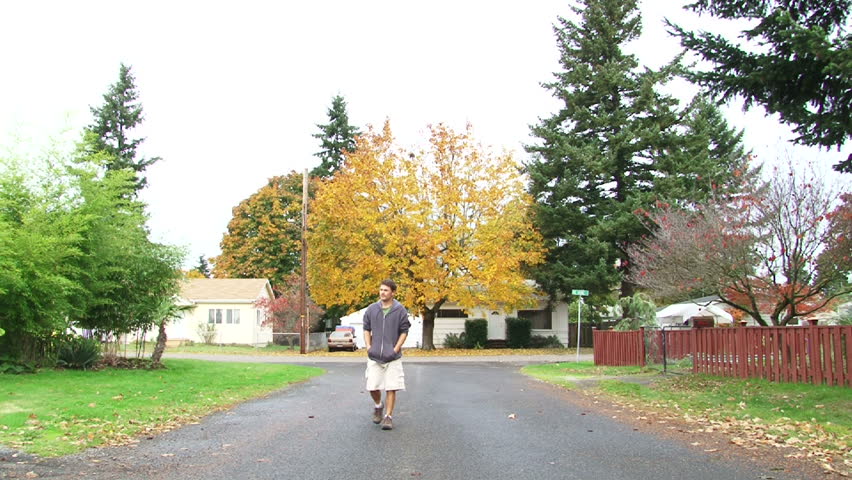 Man walks up neighborhood street passing camera.
