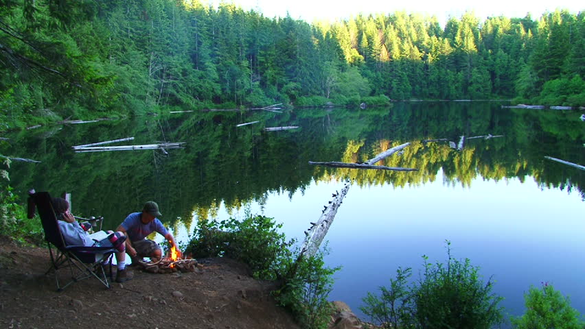 Man and woman couple enjoy peaceful lake in Oregon. Man make small campfire as