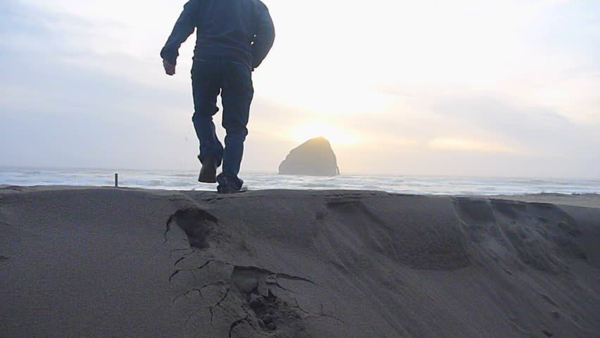 Man walking away on sandy beach to the Pacific Ocean in Oregon's coastline
