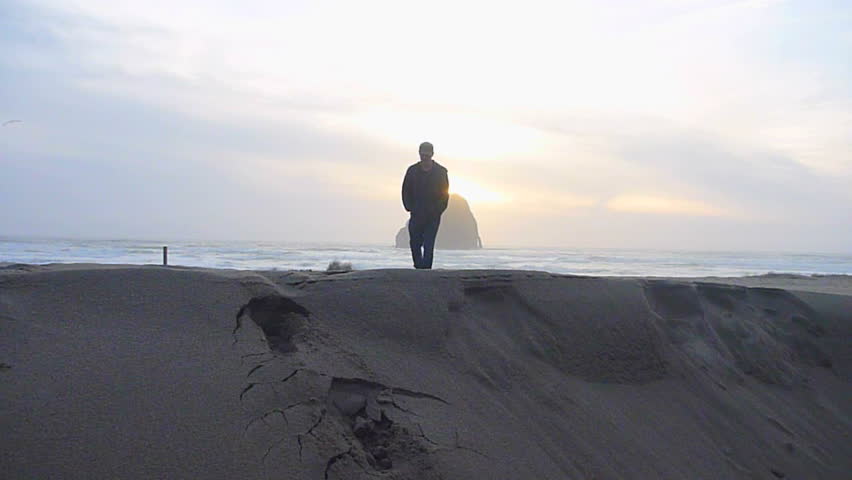 Man walking towards camera on sandy beach to the Pacific Ocean in Oregon's