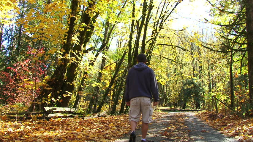 Man walks down dirt road full of fallen leaves in Oregon forest.