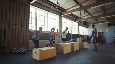 Trainer leading crossfit class on strength training exercise box jumps on wooden crates, intense workout