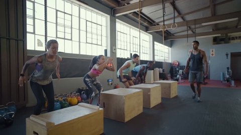 Crossfit class jumping on wooden boxes guided by trainer, strength training fitness workout in gym