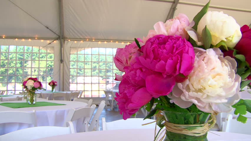 Tented wedding setting viewing large floral centerpieces .