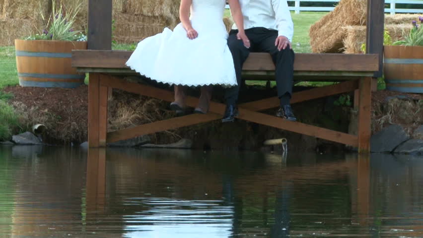 Model released bride and groom reflecting on lake as they sit together on small