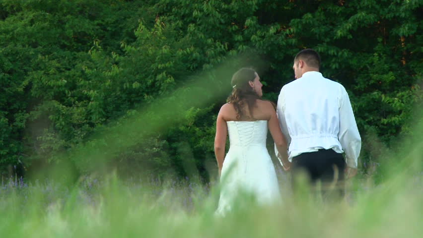 Model released bride and groom walking together towards flowers and forest on