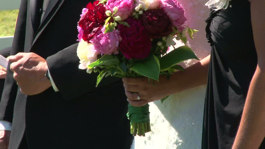 Bride standing with her parents holds her flower bouquet and wears her wedding