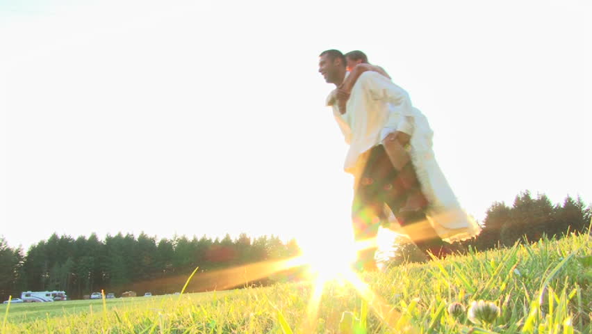 Happy bride grabs hold of her groom, and takes a piggy back ride in beautiful
