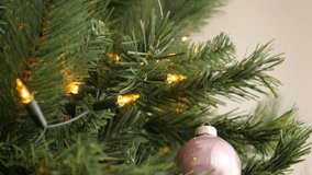 Warm yellow Christmas bulbs and pink bauble on artificial tree branches 4K 2160p 30fps UltraHD tilting footage - Close-up of tiny yellow fairy lights lighted slow tilt 3840X2160 UHD video