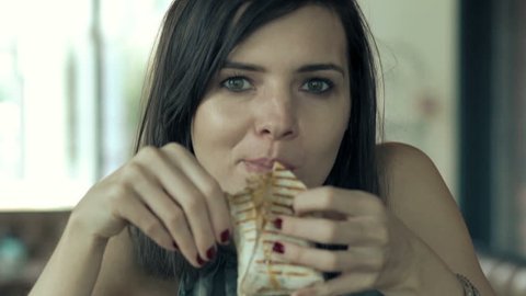 Portrait of young beautiful woman eating taco wrap in cafe
