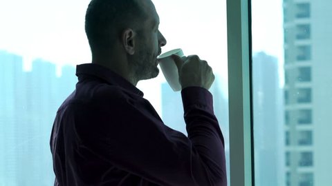 Young businessman drinking fresh coffee and admire view from window at home
