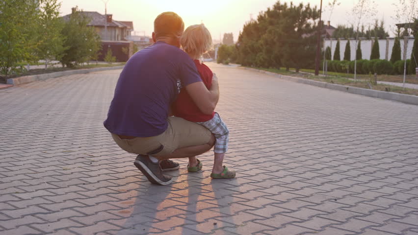 Young kid playing and his father playing with radio controlled car outside while sun setting down in slowmotion
