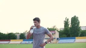 Young handsome sports man standing on stadium and drinking water