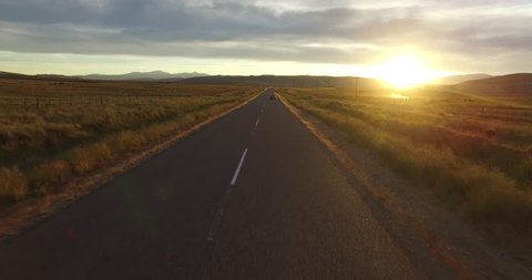 Aerial drone scene of route in steppe landscape at sunset golden hour. Camera moving forward following a tracked van on the road.