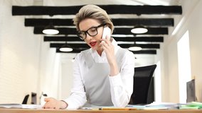 Angry irritated businesswoman sitting in her office and screaming while talking on mobile phone