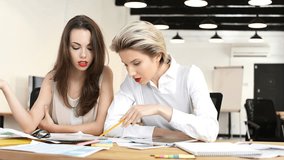 Two female colleagues working together while sitting in office at the desk