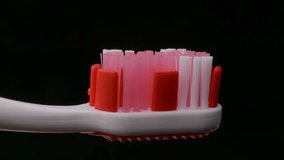 Ungraded: Tooth paste and brush. Applying green toothpaste on red toothbrush against black background. Source: Lumix DMC, ungraded H.264 from camera without re-encoding. (av34873u)