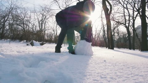 Guy making snowman rolling a huge snowball, slow motion