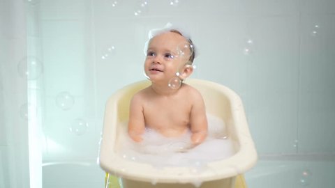 Slow motion footage of happy cheerful baby boy playing at bathtub