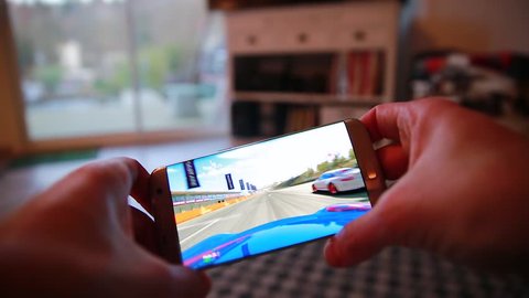 Paris, France, January 25, 2017: Man Playing Real Racing 3 (EA Games) Video Game On His Modern Smartphone Samsung Galaxy S7 Edge At Home
