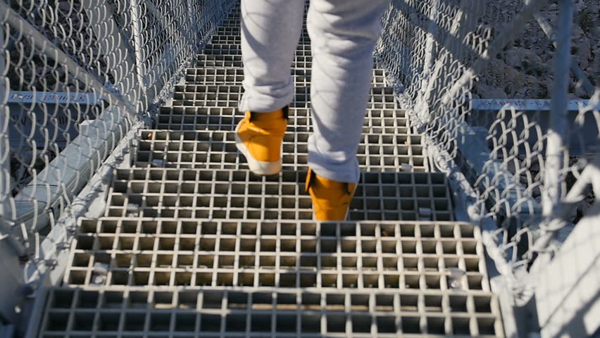 go down the stairs - Human feet in yellow sneakers are going down the metal stairs of the bridge