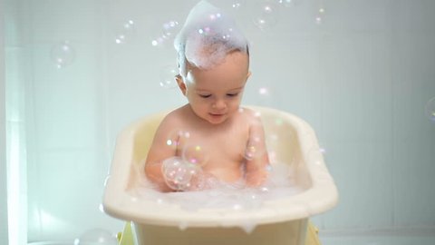Slow motion footage of cute baby boy playing in bathtub with suds and soap bubbles