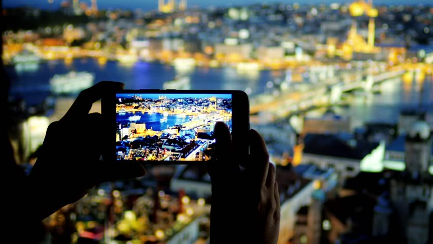 Woman takes a picture of  night Istanbul with smartphone camera.