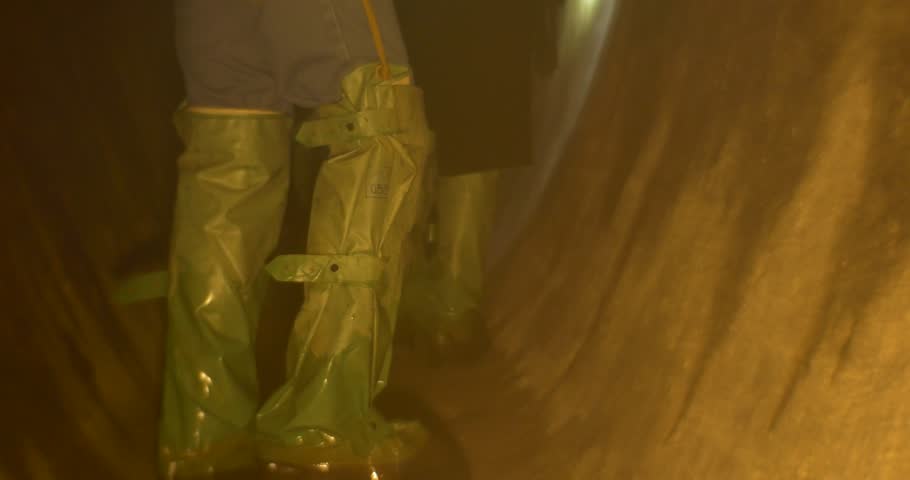 an Enigmatic and Semidark Mine Tunnel and Several Men, Dressed in Chemsuit Boots, Jeans, Cotton Jackets, Hard Hats, and Backsacks, Who Light up Their Way With Powerful Flashlights. the Legs of One