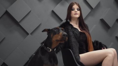 Sexy girl with long hair in black fur coat sitting near dog in studio. The dog yawning