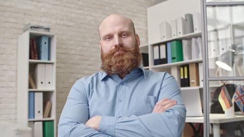 Businessman with red beard sitting with crossed arms in office chair and nodding his head while listening to somebody during video call