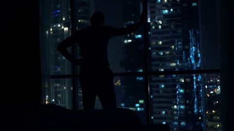 Silhouette of man having problems with sleep, waking up and standing by window at night
