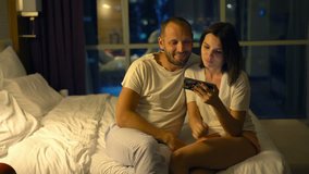 Young couple watching movie on smartphone lying on bed at night

