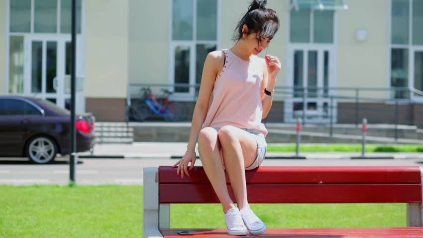 Central Asian girl poses on bench near house at summer sunny day
