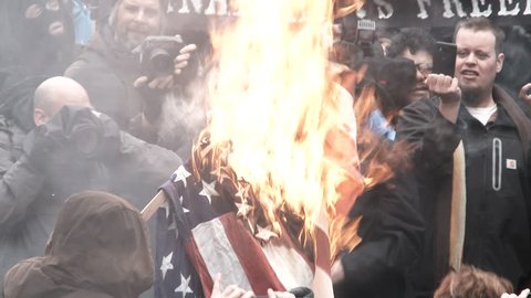 PORTLAND, OREGON - CIRCA 2017: Large group of protesters gather in downtown Portland, Oregon and burn the American flag to demonstrate their first amendment rights against Donald Trump taking office.