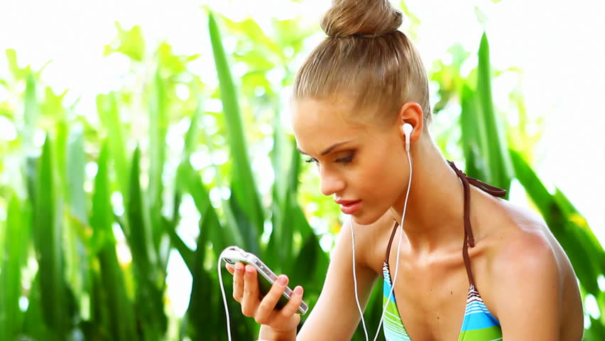 Vivacious woman in a bikini sitting on a deck enjoying the music on her digital
