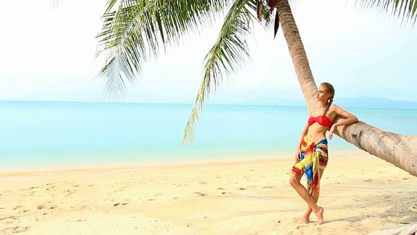 Pretty woman at the tropical beach standing next to palm tree
